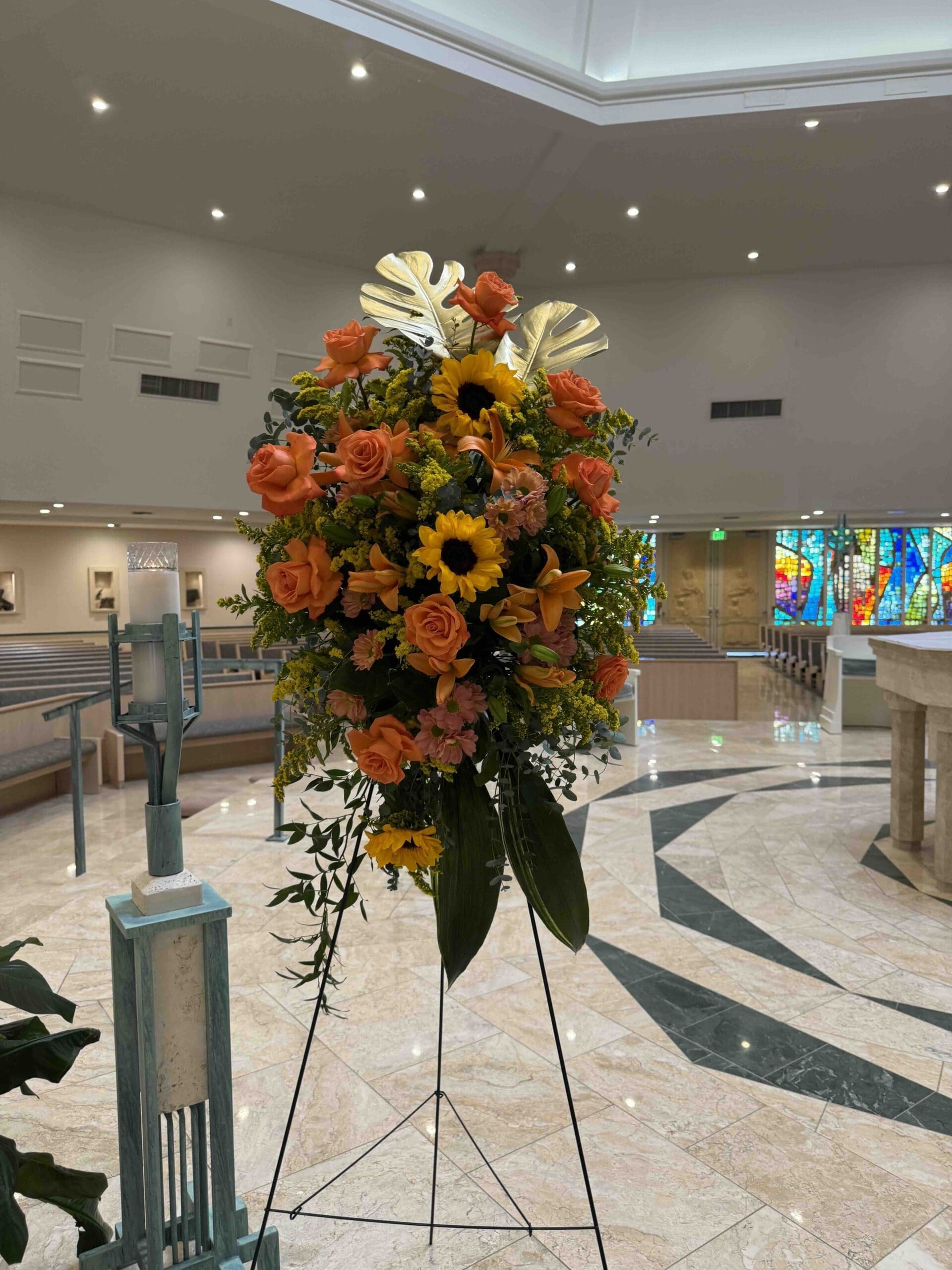 Funeral Spray Orange and gold funeral standing spray with roses, sunflowers, lilies and gold tropical leaves in Naples Florida.