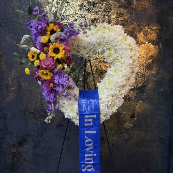 Colorful open heart funeral spray with white flowers, sunflowers, purple stock and pink roses in Naples Florida.