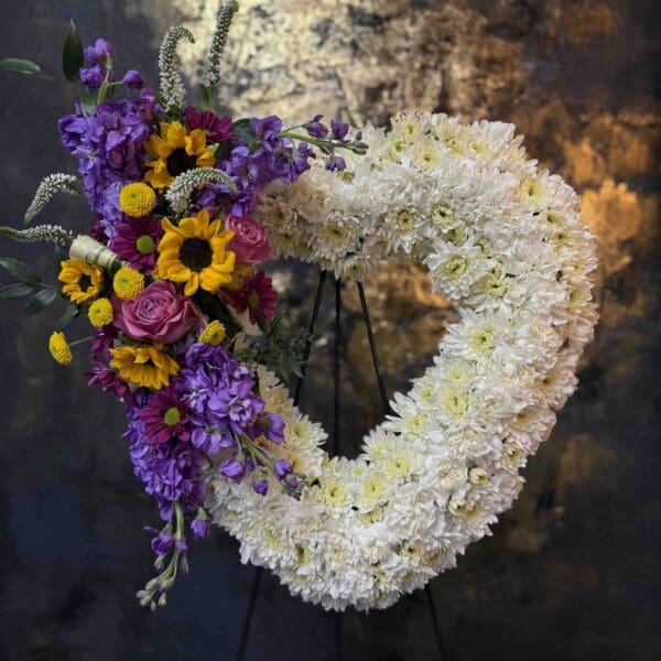 Colorful open heart funeral spray with white flowers, sunflowers, purple stock and pink roses in Naples Florida.
